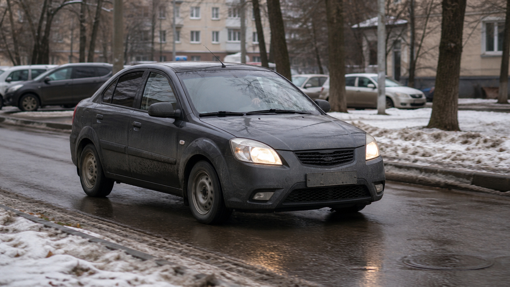 Автомобиль едет по мокрой зимней дороге рядом с талым снегом